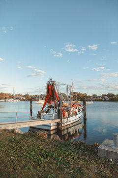 Fishing trawler docked at a pier with sailboats in the background under a blue sky
