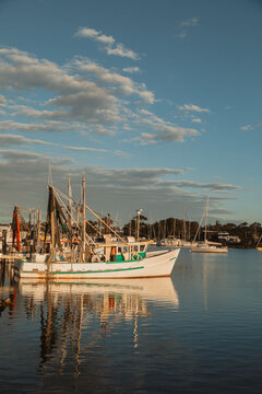 Fishing trawler docked in a calm harbour reflecting in the water at sunset