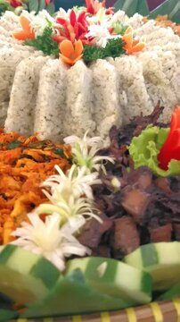A vibrant and detailed view of Indonesian Tumpeng Nasi Daun Jeruk (Lime Leaf Rice) surrounded by traditional side dishes, decorated with beautiful vegetable carvings and garnishes