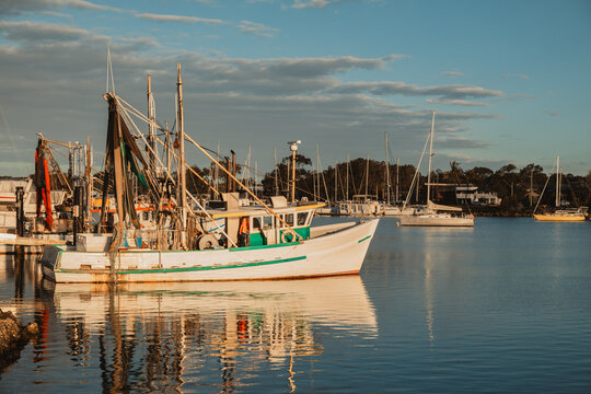 Fishing trawler docked in a harbour with sailboats and calm water at sunset