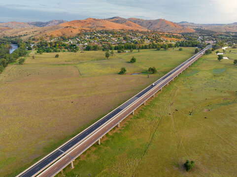 Aerial view of an elevated freeway through green farmland in front of hills in golden lighting