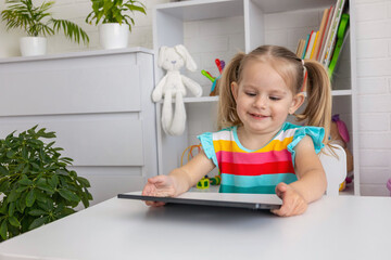 Little girl with pigtails using tablet in a playroom. Technology and childhood. © Anna