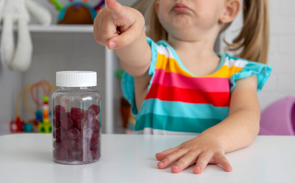 Little child pointing finger at bottle of vitamin gummies or fruit candies.