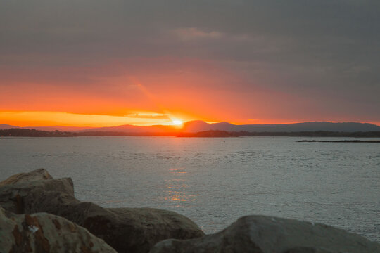 Dramatic sunset over the ocean with sun rays breaking through clouds and silhouetted hills