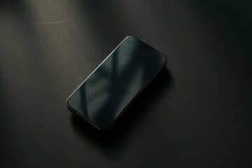 黒デスクに置かれた黒いスマートフォン 画面オフ ミニマルな真上俯瞰 モックアップ背景素材 / Black smartphone with black screen on dark wooden desk, top view, minimal flat lay, mockup background © takayuki