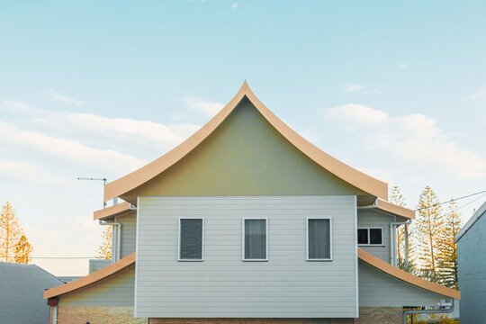 Modern house with unique curved roof design against a clear blue sky with clouds