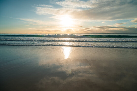 Waves breaking under vibrant sunrise with reflections on wet sand