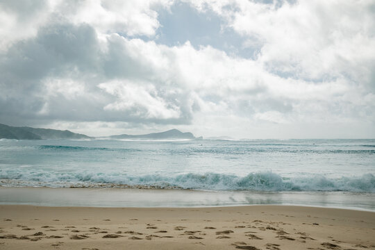 Dramatic cloudy sky over a rugged coastline with crashing ocean waves and sandy beach
