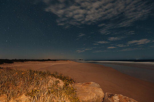 Vast beach under a starry night sky with gentle waves lapping the shore