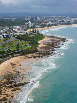 Aerial view of rain falling from dark clouds over a rocky coastline and distant waterfront buildings