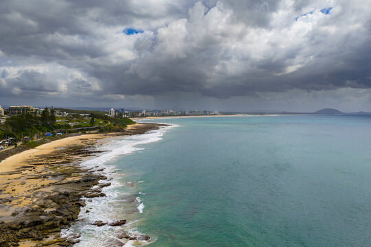 Aerial view rain falling from dark storm clouds over a calm bay and rocky coastline