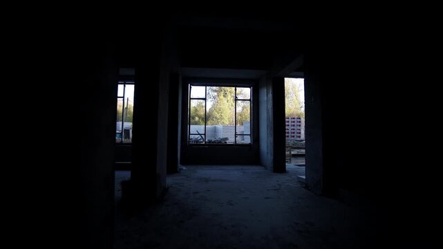 Long dark corridor inside incomplete apartment building with large windows. Walking along lobby to entrance without glass at construction site