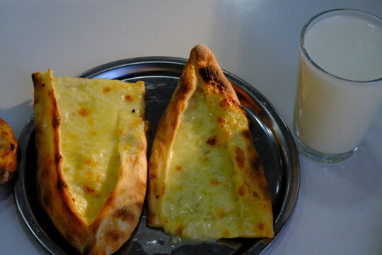 Close-up view of a pide Turkish flatbread with Kashar cheese. A glass of ayran yogurt drink. Ramadan pide. Iftar meal. Traditional Turkish cuisine. Hot, freshly baked pide. Healthy eating.