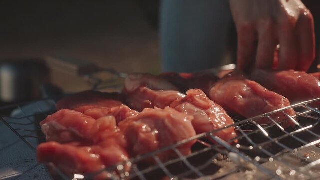 Raw chicken on grill camping prep, closeup of hands arranging pieces on metal grate over charcoal, dusk glow, smoky warmth, textured meat, careful placement, intimate outdoor cooking scene
