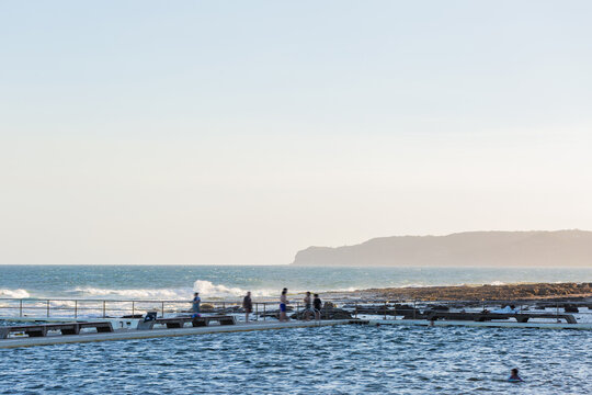 Merewether ocean baths shaded by seaside cliffs in the afternoon with big sky