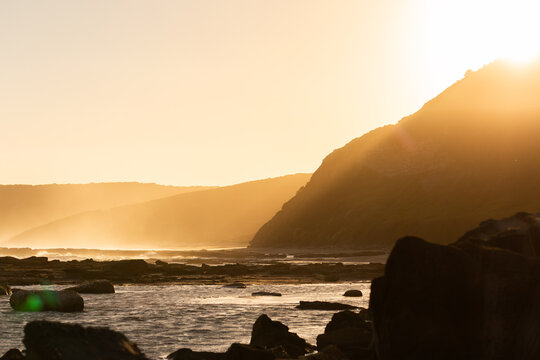 golden light streaming down through sea spray from ocean cliffs to rocky shore