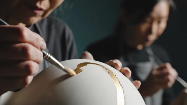 Mastering the Art of Kintsugi with a close-up of hands applying gold lacquer to repair white ceramic pottery, ideal for traditional craftsmanship documentaries and mindfulness content.