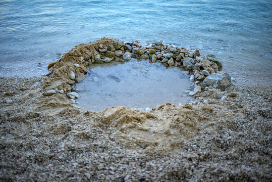 Stone-lined sand pool on pebbly beach by calm sea