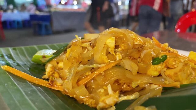 Pad Thai noodle dish served at an outdoor Thai street food court, close-up of authentic stir-fried noodles.