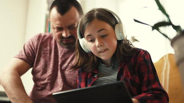 Preteen girl in headphones showing interesting content on digital tablet to her father at home-4k,10 bit footage.