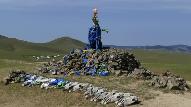 Sacred pile of stones (ovoo, obo) on the background of low mountains and blue sky. Yurts in distance. An offering in the form of skulls of Pets in front of obo. Mongolian landscape. Summer sunny  day.