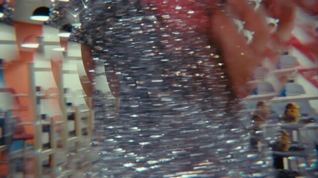 Close up of a girl in a shimmering silver sequin dress dancing at a vibrant party. The scene has a dreamy, distorted effect with red streamers and a blurred, stylish background