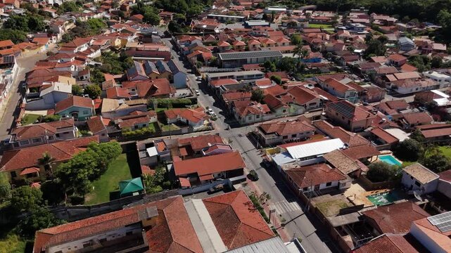 Aerial view of residential area with red tile roofs, houses, streets, pools and solar panels surrounded by green mountains in Sao Bento do Sapucai, Brazil. Push in and tilt up camera movement