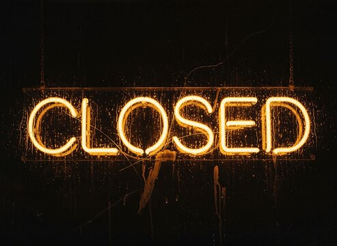 Glowing neon closed sign in warm amber light, vintage electric glass tube signage on dark background, illuminated business closed notification