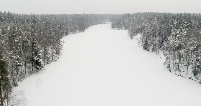 Aerial view of snow-covered landscape of frozen Kaitalampi lake winding through a dense, snow-draped boreal forest in cloudy winter weather, Espoo, Finland, Europe.
