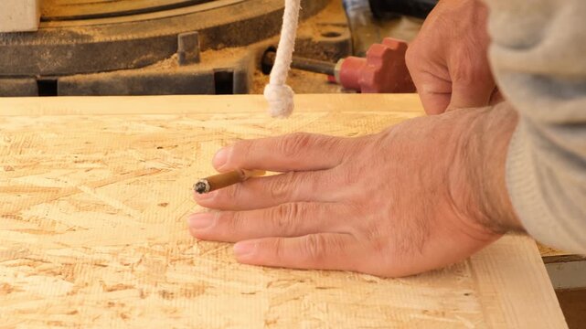 Furniture craftsman fitting new door hinges on cabinet door while holding a smoldering cigarette. Safety violation in woodworking workshop. Fire hazard when working with wood.