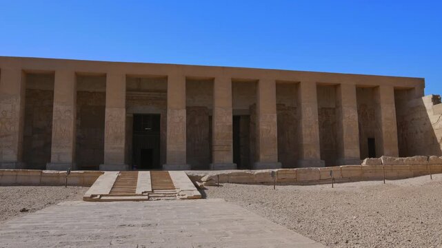 Abydos Temple of Seti I facade with grand stairway and colonnade in Egyptian desert. One of Egypt's most sacred ancient sites under vivid blue sky. Egypt.