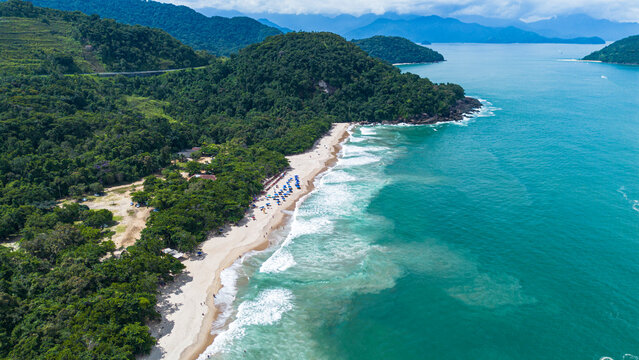 Aerial drone view of Felix Beach in Ubatuba, Brazil. Beautiful tropical coastline with turquoise water, white sand and lush green rainforest under a bright sunny blue sky.