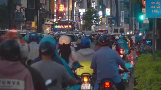 Hundreds of bikes on the busy night road of Saigon slowly move in the traffic jam towards neon lights on the skyscrappers. Ho Chi Minh, Viet Nam