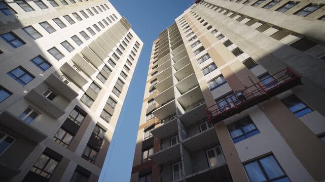 Highrising residential buildings with balconies panels under blue sky. Constructing multistory apartment facility in new urban district
