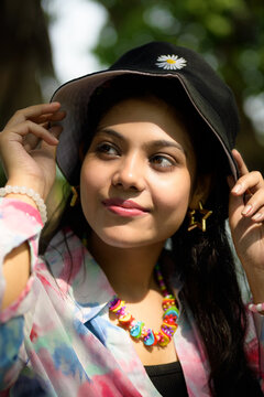 Stylish young Indian woman wearing a casual outfit with a hat and vibrant accessories, posing outdoors in natural daylight