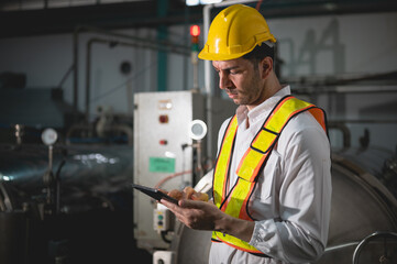 Industrial engineer inspecting machinery and monitoring pressure gauge in a factory. The engineer uses a tablet for maintenance and quality control.
