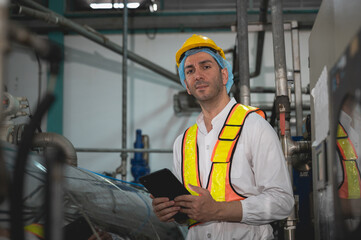 Industrial engineer inspecting machinery and monitoring pressure gauge in a factory. The engineer uses a tablet for maintenance and quality control.
