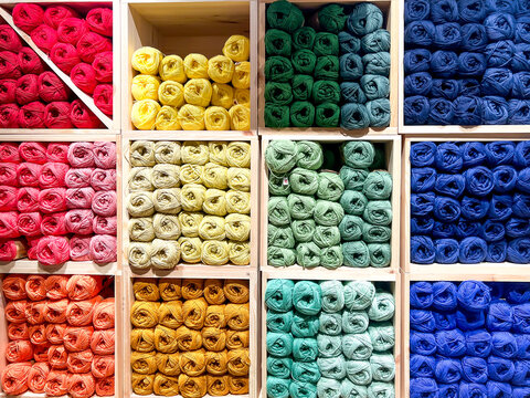 Balls of wool of many colours neatly arranged and on sale in a haberdashery shop, stored in a storage unit divided into cubes