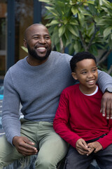 Obraz premium African American father and child sitting on stone ledge at patio, wearing grey sweater, wristwatch