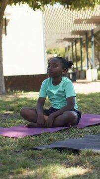 Vertical video: Sitting on purple mat in park, girl bringing palms to chest and meditating in tee