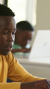 Male student placing hands on laptop keys, typing in class completing work, classmate working