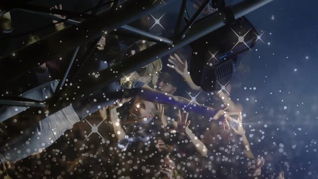 Attendees supporting crowd-surfer at music concert, arms rising, confetti falling, lights flaring