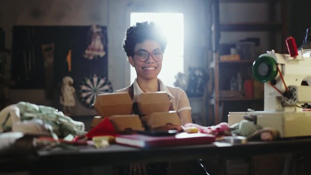 A person is working on a sewing project in a workshop. They are smiling and creating items while surrounded by fabric and tools. The light shines through the window.