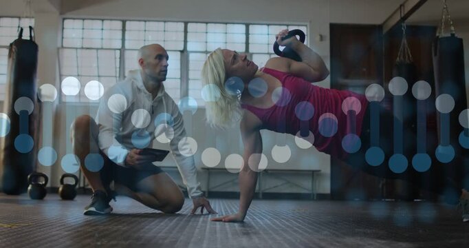 Fitness coach tapping tablet cueing woman doing kettlebell rowpress, timing, bokeh overlay showing