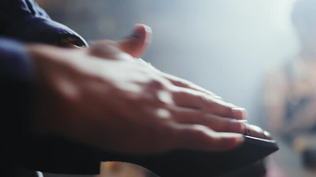 A person is carefully polishing shoes in a dimly lit shop. The hands are focused on the task, rubbing the shoe to bring out its shine. The atmosphere is busy but quiet.