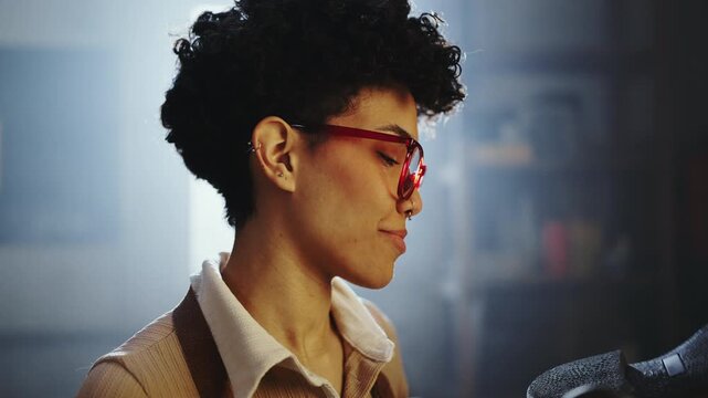 A person with curly hair and red glasses focuses on their work. They are in a workshop surrounded by tools and equipment, preparing for a creative task in the afternoon.