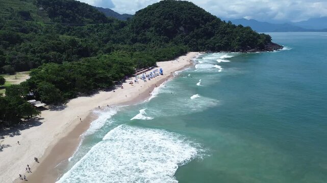 Aerial drone view of Felix Beach in Ubatuba, Brazil. Beautiful tropical coastline with turquoise water, white sand and lush green rainforest under a bright sunny blue sky.