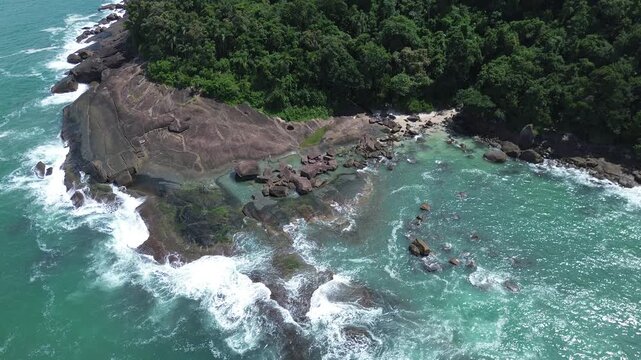 Aerial drone view of Conchas Beach and rocky coastline in Ubatuba, Brazil. Tropical turquoise water, sea shells sand and lush green rainforest under a bright sunny sky in Sao Paulo.