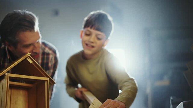 A man and a boy work on a project in a workshop. They focus on creating a model. The boy holds pieces and listens to the man as he guides him.