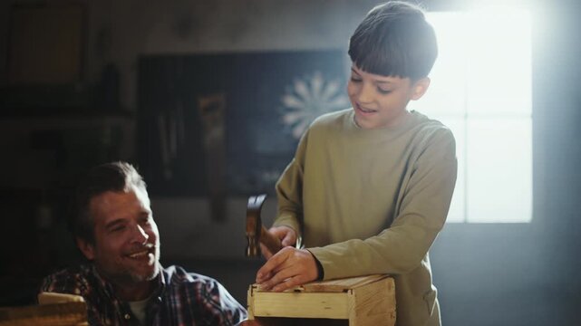 A father teaches his son how to build a wooden box in a workshop. They use tools and share smiles as they create something together. The atmosphere is filled with learning and joy.